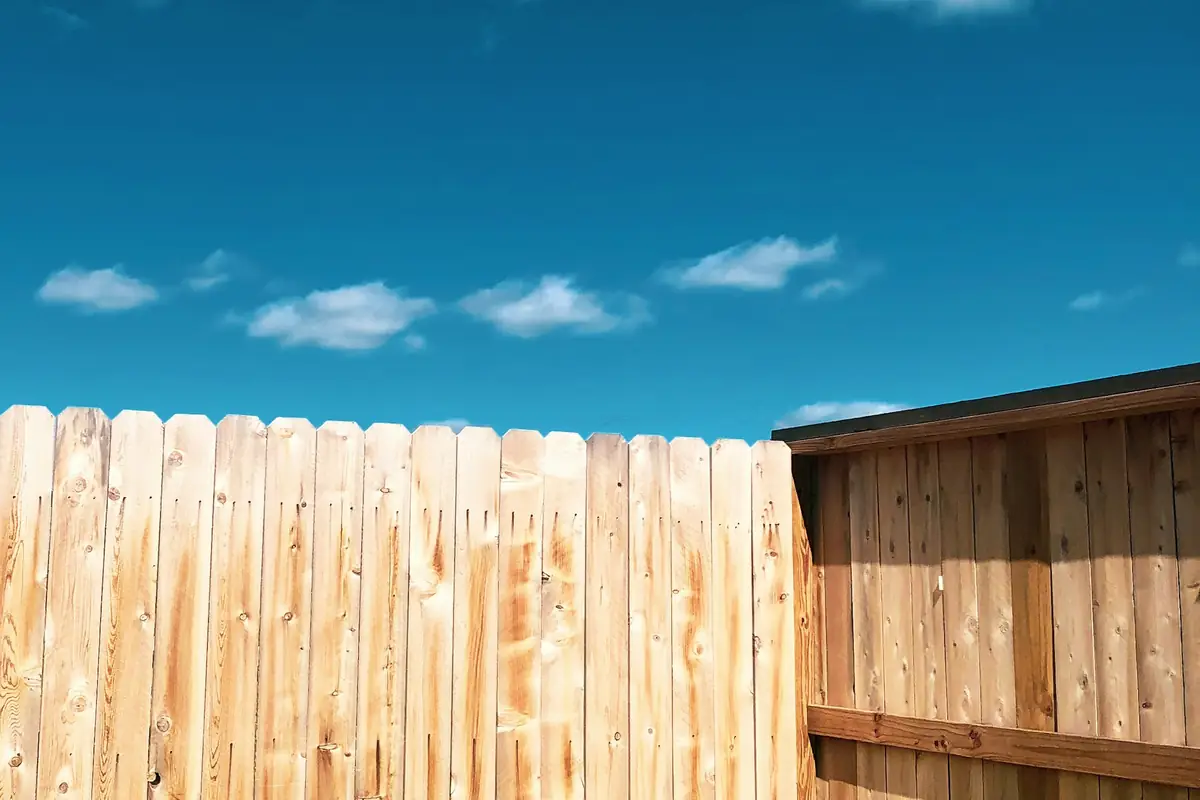 The top of a dog-ear wooden privacy fence against a blue sky